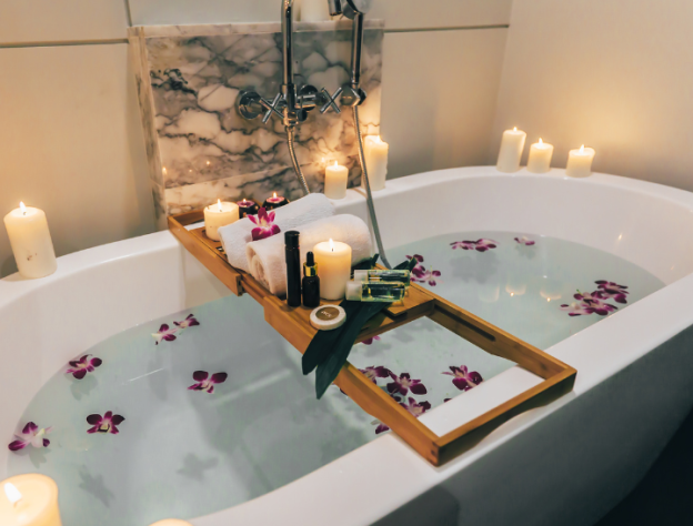 image of a bathtub filled with petal and multiple candles lit around with bath board filled with products